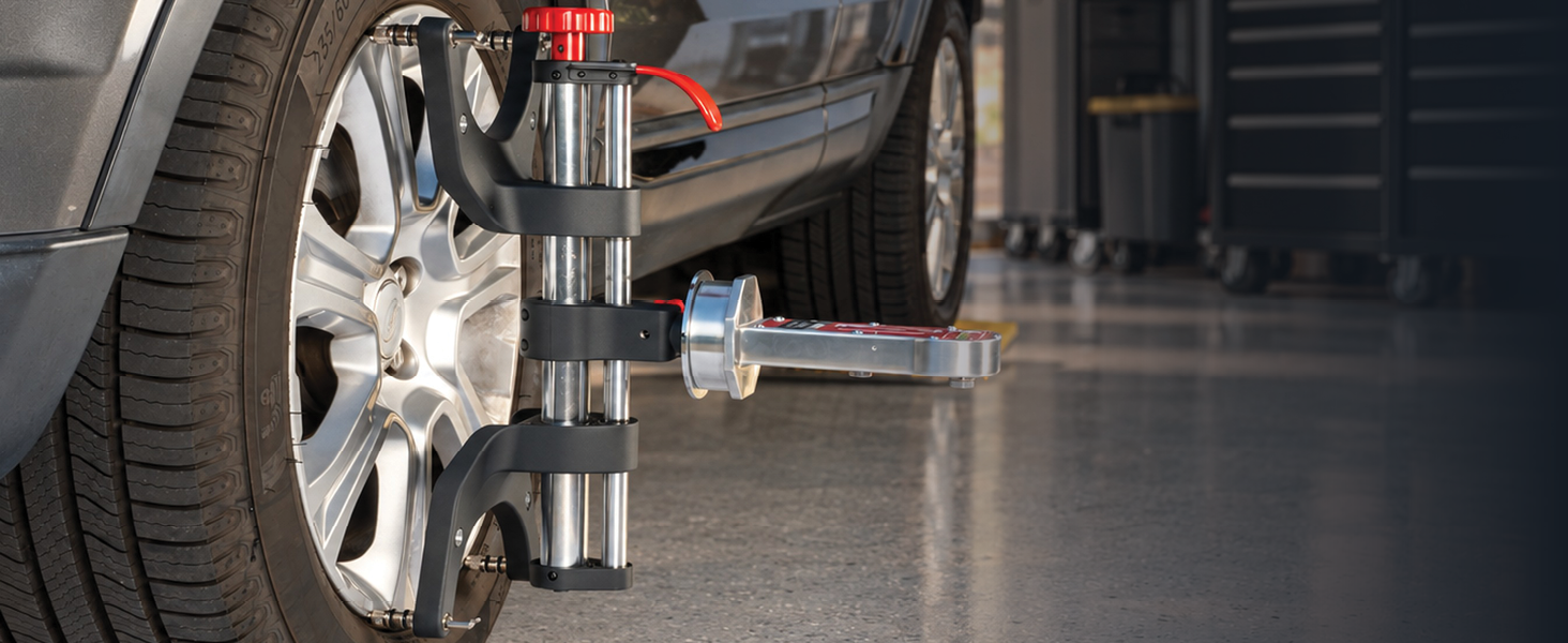 AutoSolo ONYX PRO wheel clamp mounted on a car wheel in a garage, a camber caster gauge docked on the adapter plate