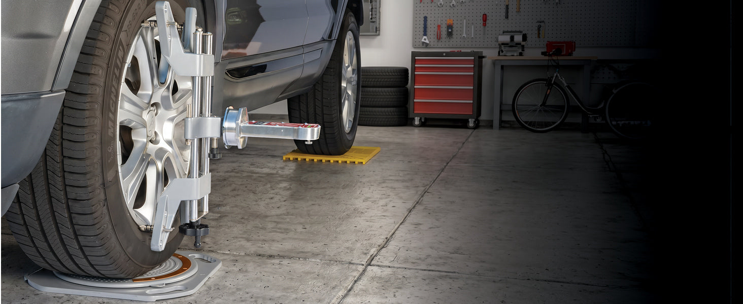Car staged in a home garage on AutoSolo turn plates and ramps with a wheel clamp and alignment gauge mounted to the front wheel